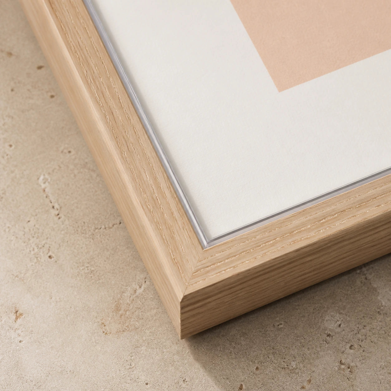 Close view of a pale wood frame corner beside a white art surface